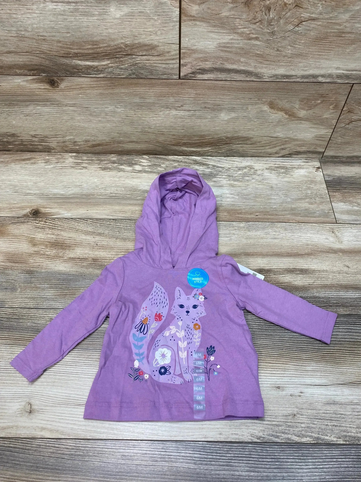 Flat lay of NEW Carter Hooded Shirt in purple sz 6m showcasing fox and flower graphic with hangtag on wood plank background