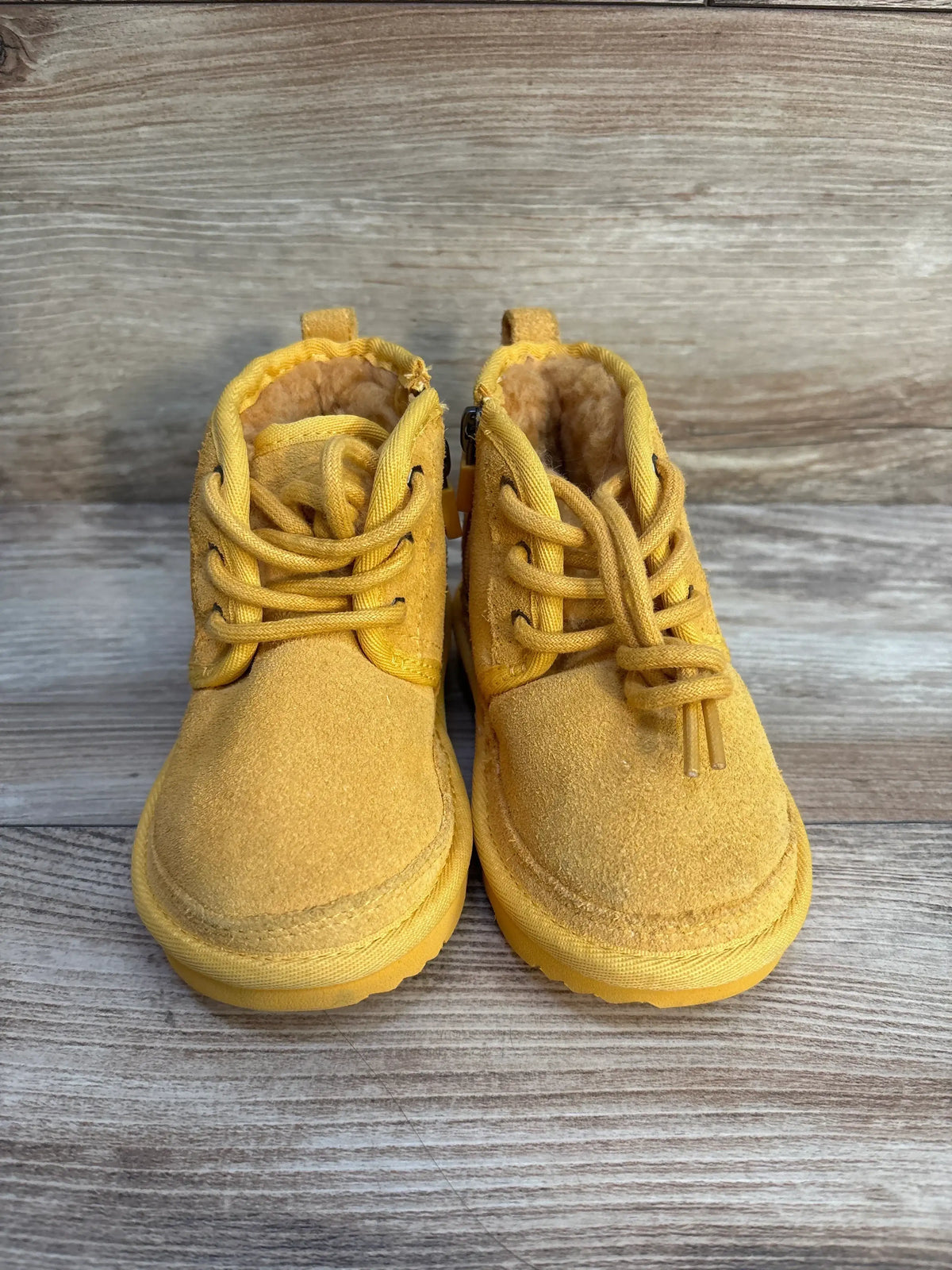Front view of Ugg Neumel II toddler boots (size 8C) showcasing yellow suede, lace-up design and shearling lining on wooden floor