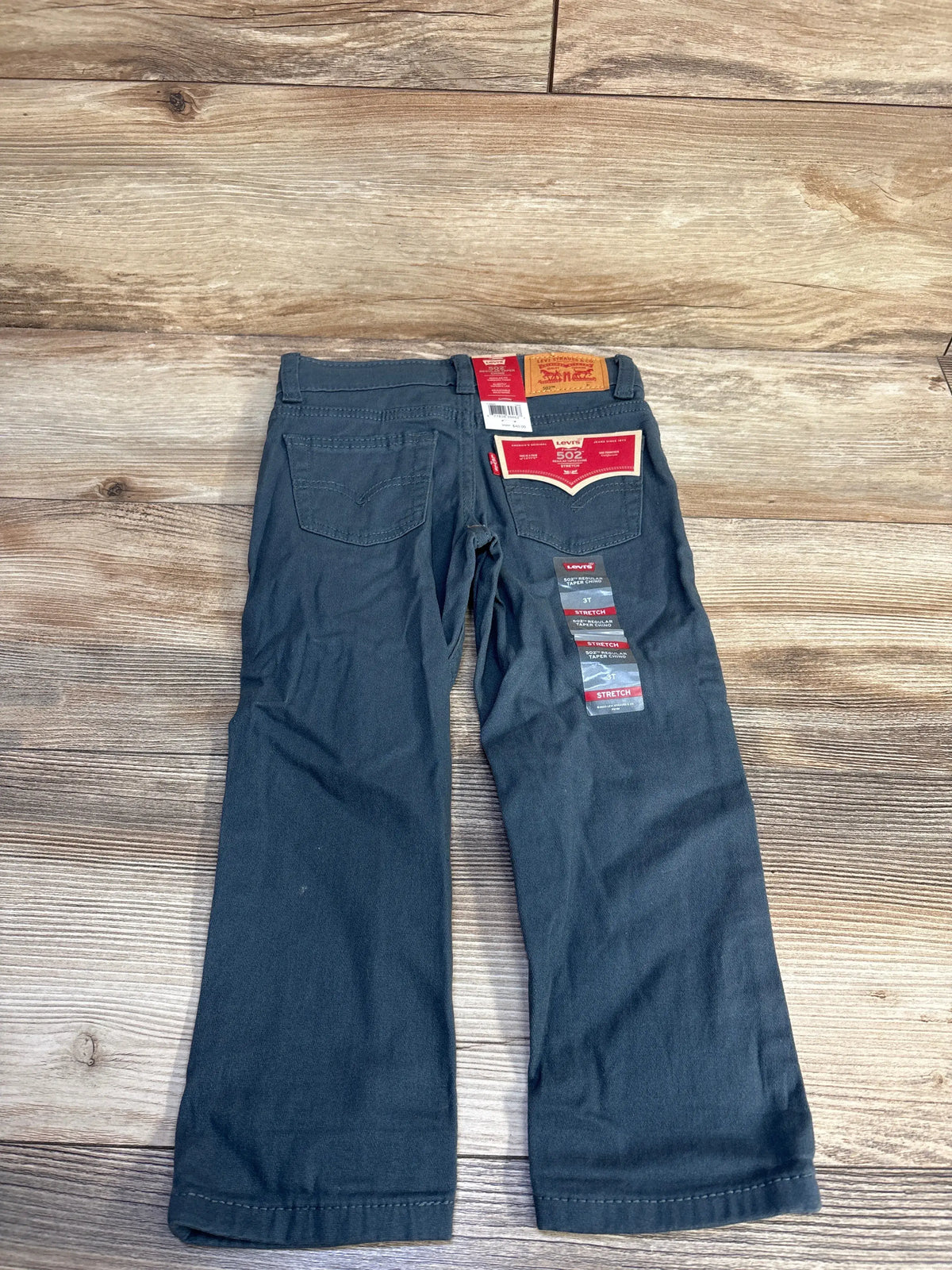 Back view of grey Levi’s 502 Regular Taper chino pants showcasing back pockets and 3T tag on wood background