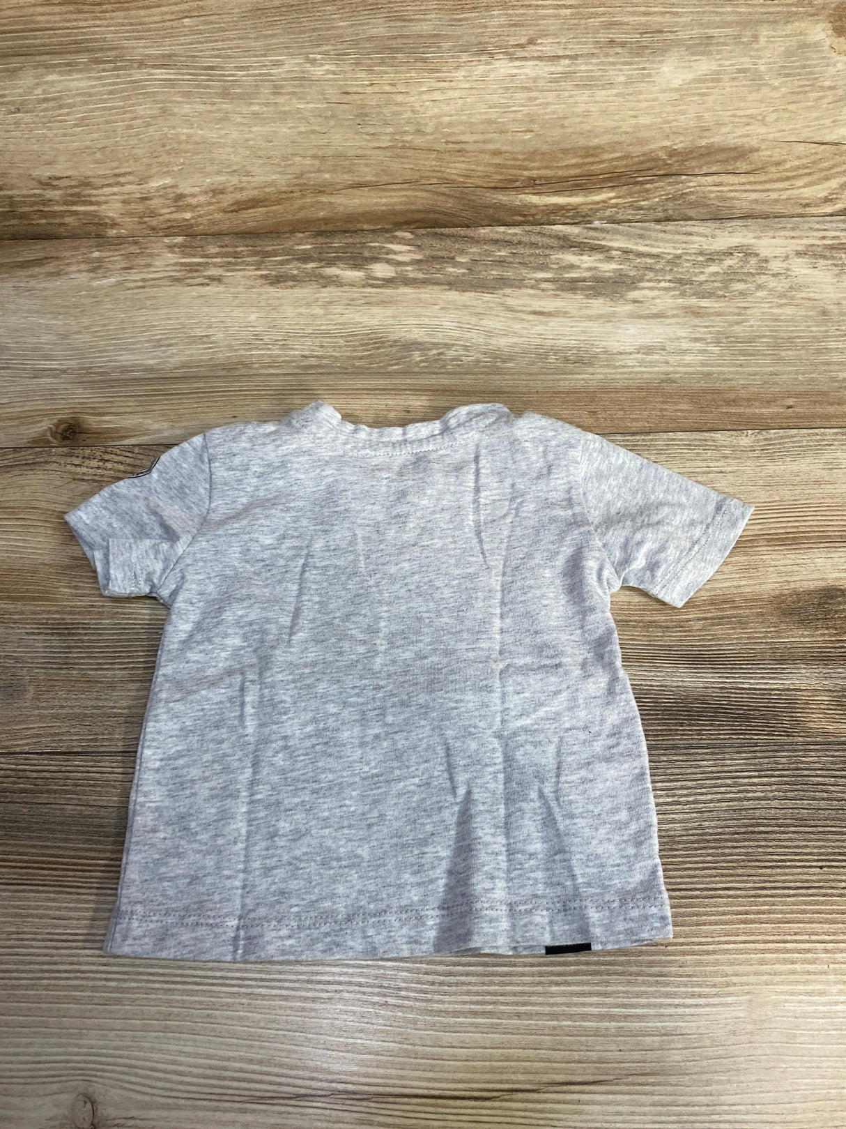 Back view of a light gray toddler t-shirt on wood background