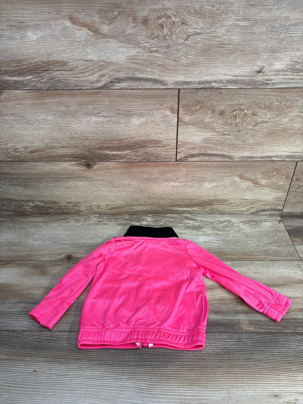 Back view of a bright pink jacket with a black collar on wood flooring