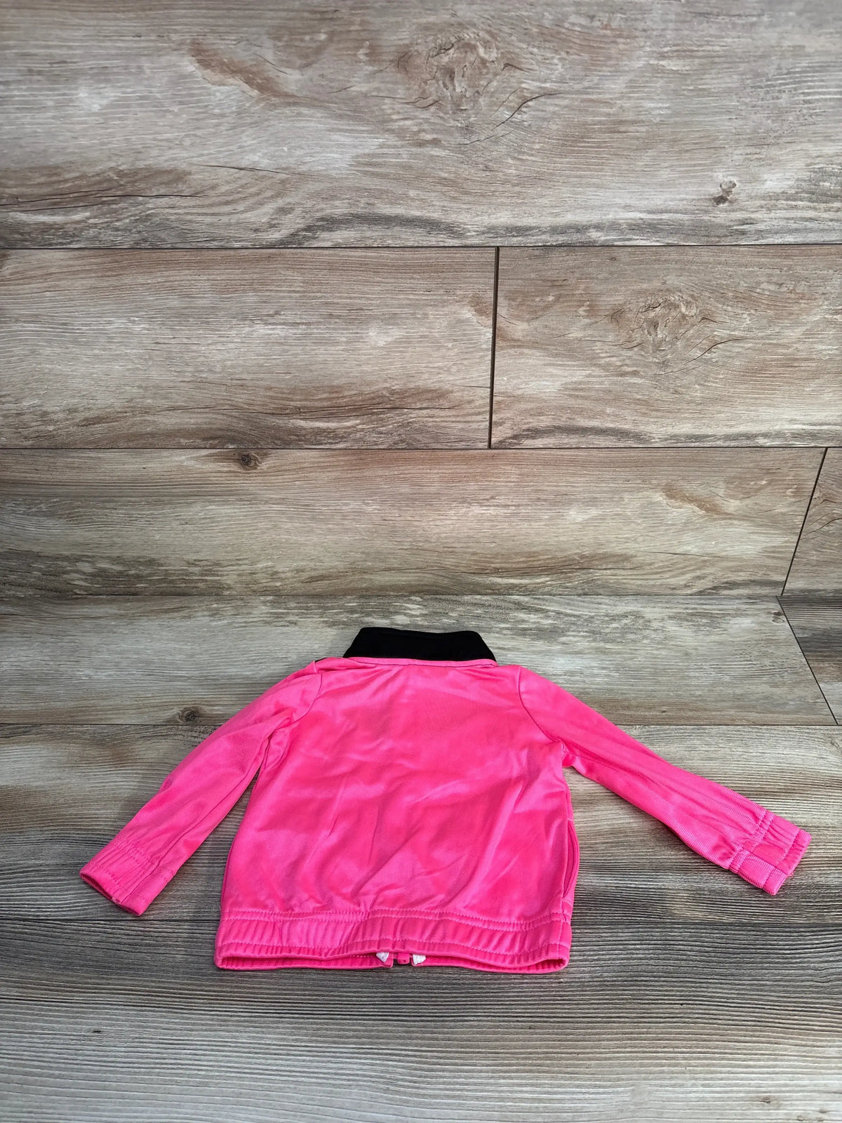 Back view of girls’ Puma full-zip jacket in hot pink showing black collar, long sleeves, and elastic hem on wood floor