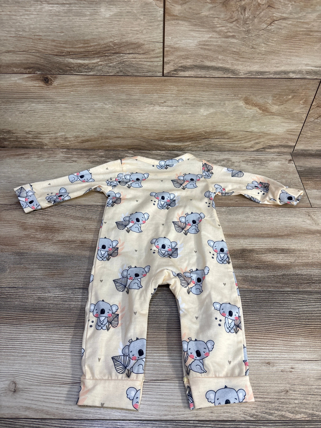 Flat lay of yellow koala coverall showing all-over koala print, long sleeves and fold-over cuffs on wood background