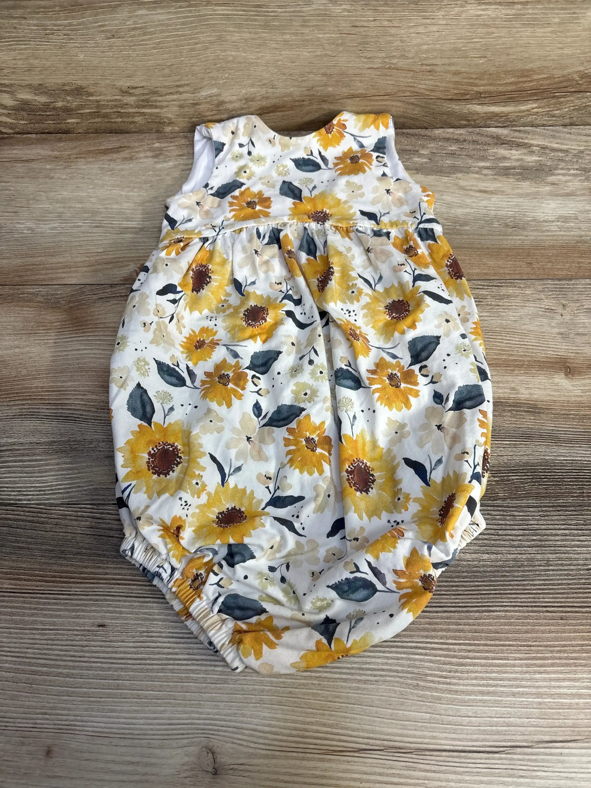 Flat lay of white 4T toddler romper with yellow sunflower print, gathered waist and elastic leg openings on wood background