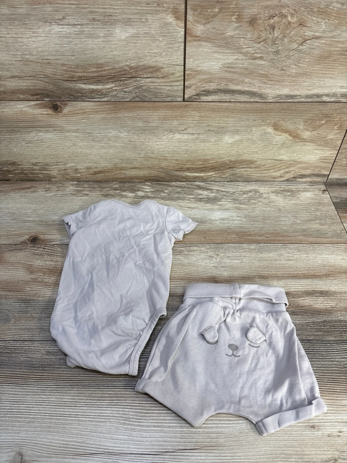 Flat lay of beige 2-piece baby kimono bodysuit and foldover shorts showing bear face on shorts on light wood background