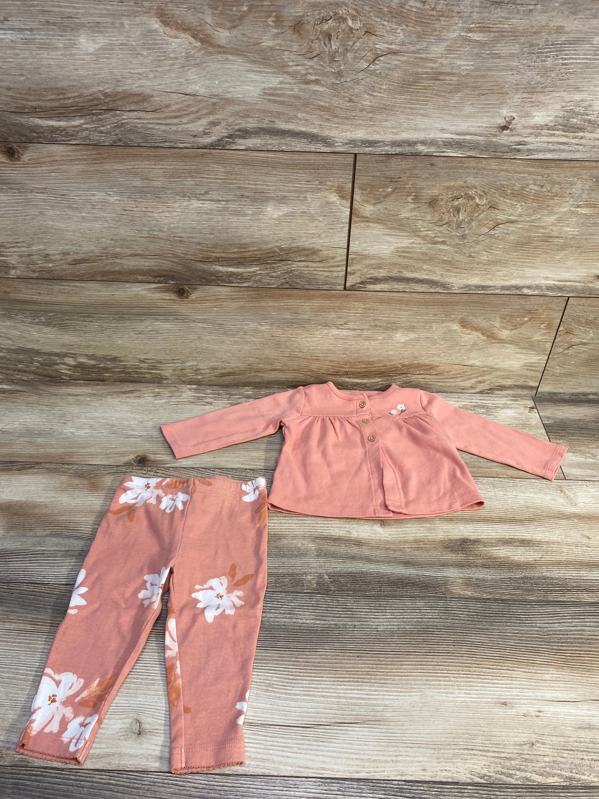 Flat lay of 2-piece Carter’s set showing pink button-front long-sleeve top with small embroidered flower and matching floral leggings on wood background