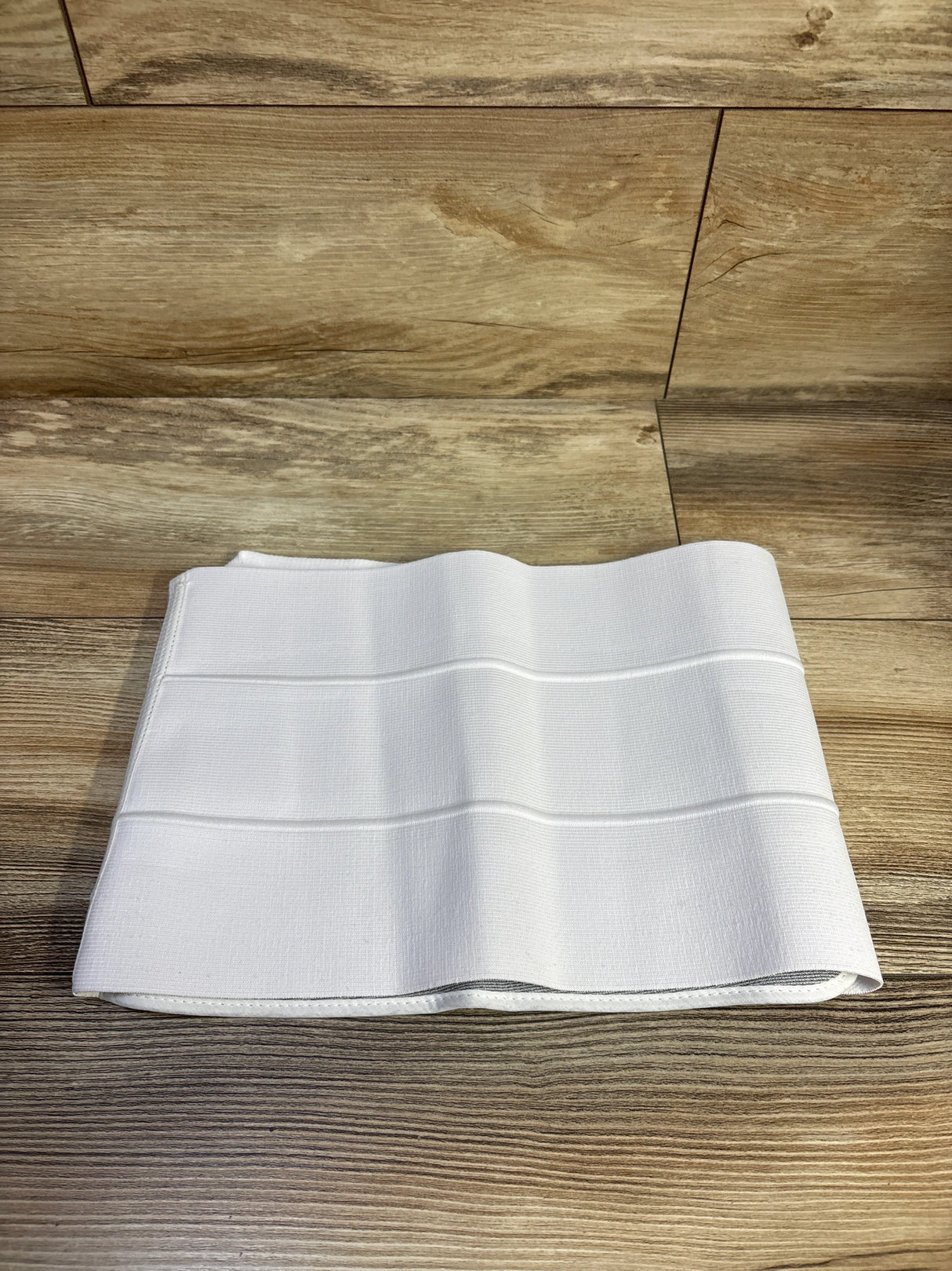 Top down view of Breg 9 inch abdominal binder folded to show elastic ribbing and hook and loop edge on wood background