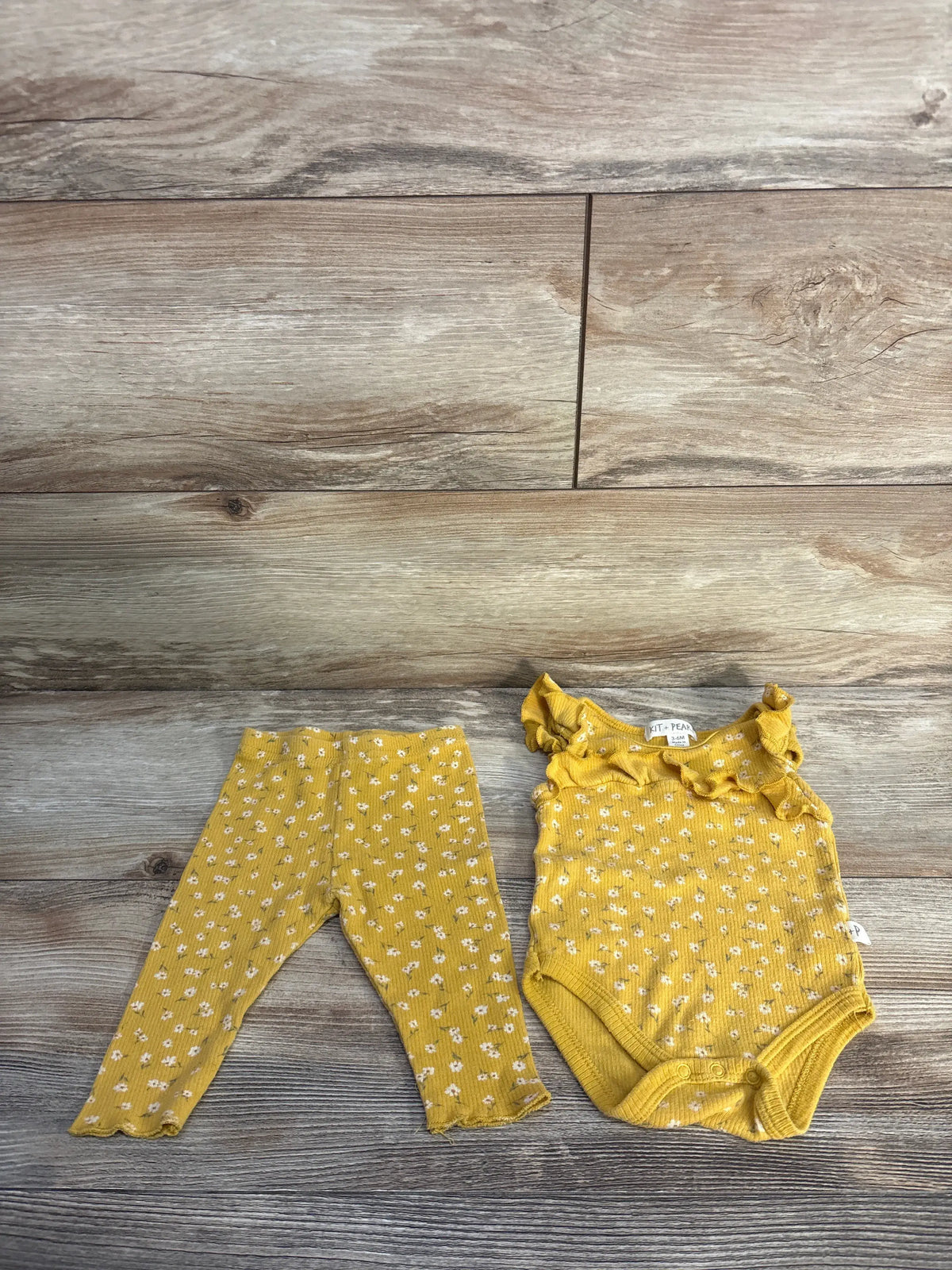 Top view of yellow Kit + Pearl ribbed bodysuit and pants set with floral pattern on a wood floor