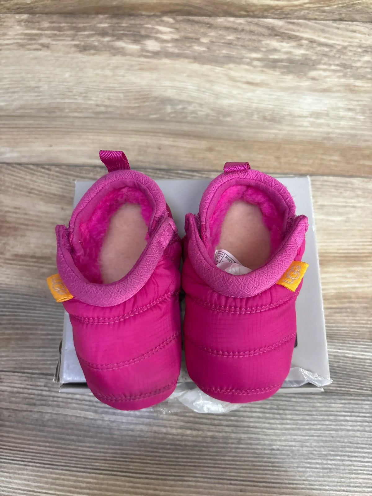 Pair of pink UGG toddler boots with plush lining on white box over wooden floor