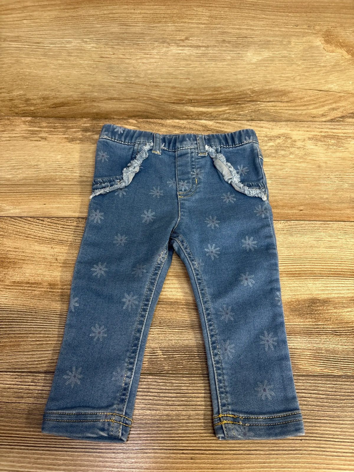 Toddler blue denim jeans with floral print and frayed pocket trim on wooden surface