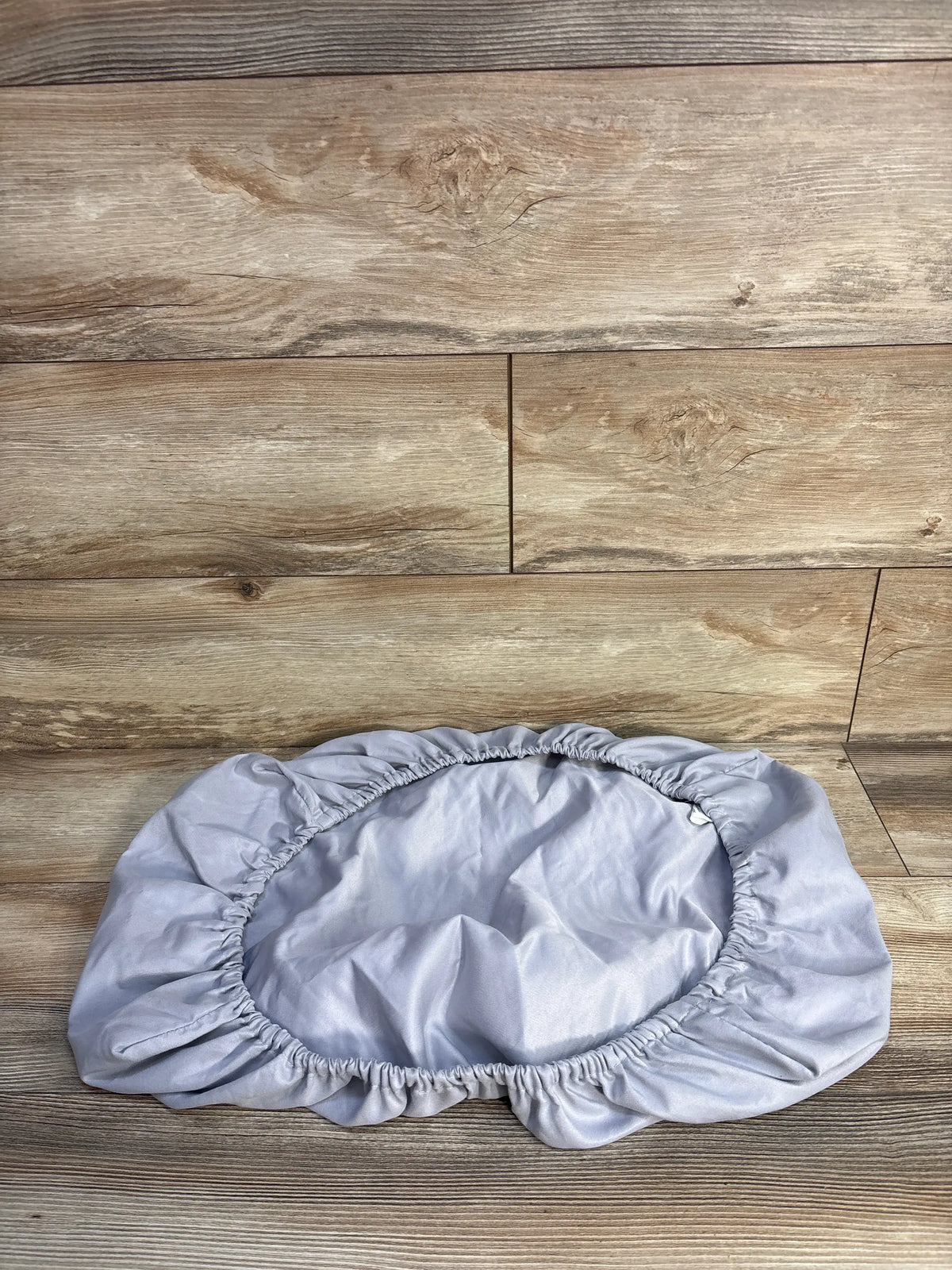 Top-down view of Parent’s Choice fitted bassinet sheet in grey showcasing elasticized fitted edge on wood plank background