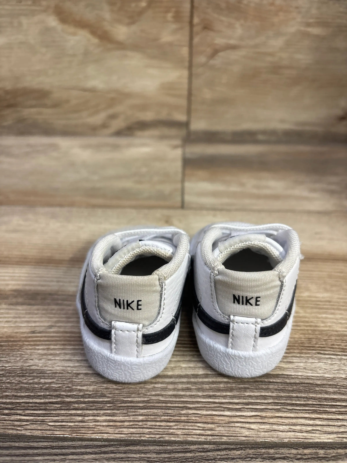 Rear view of Nike Blazer Mid CB sneakers showcasing white uppers, black accents, and Nike heel branding on a wood surface