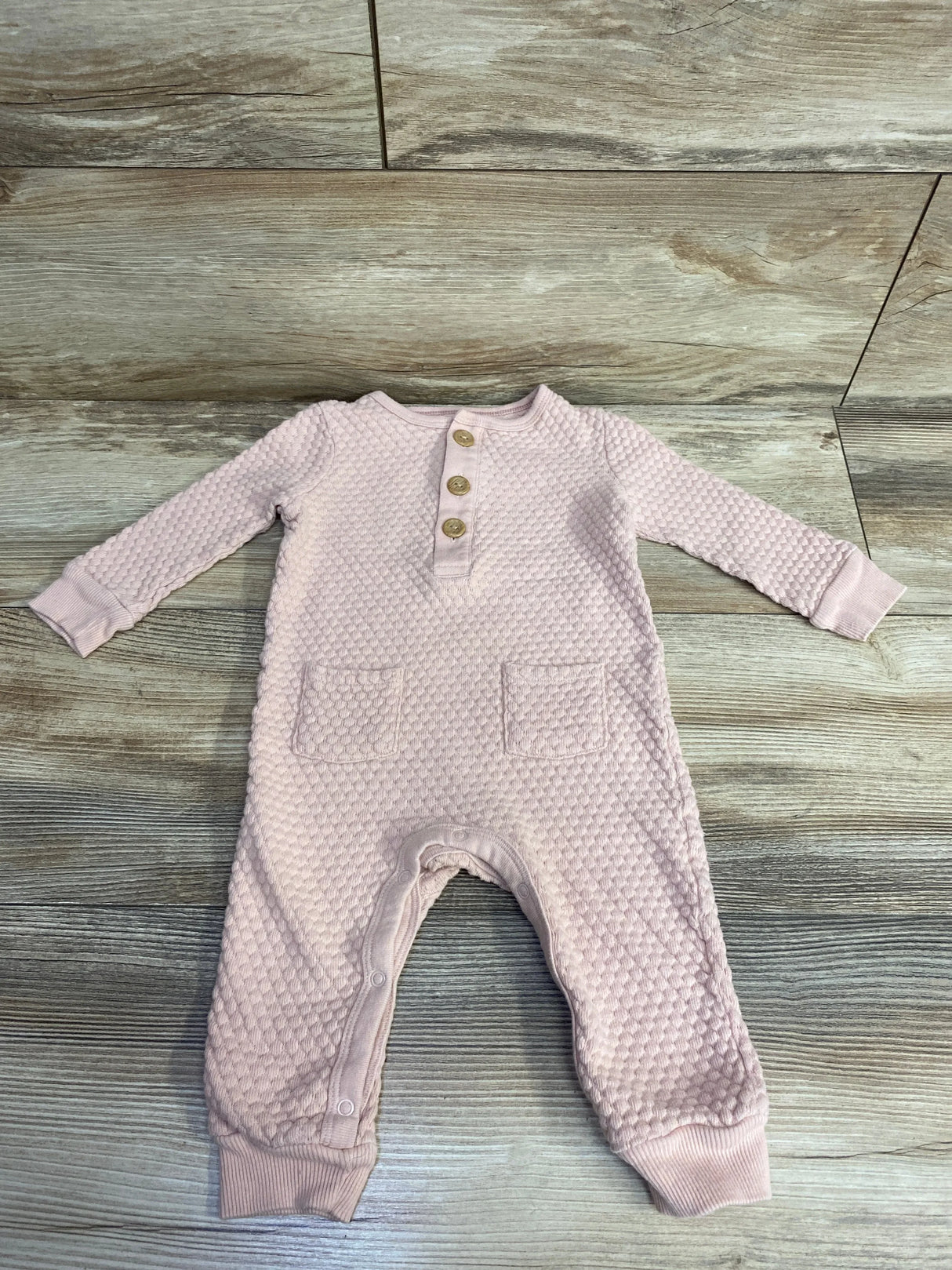 Textured pink baby romper with wooden buttons and front pockets on wooden background
