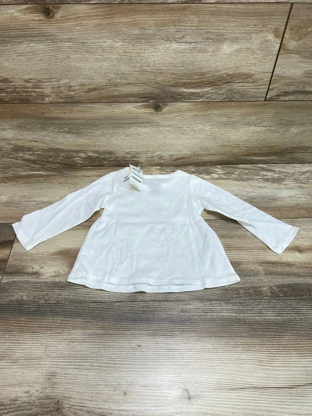 Flat lay of white baby long-sleeve First Impressions shirt (12 months) showing faint deer graphic and gathered waist on wood background
