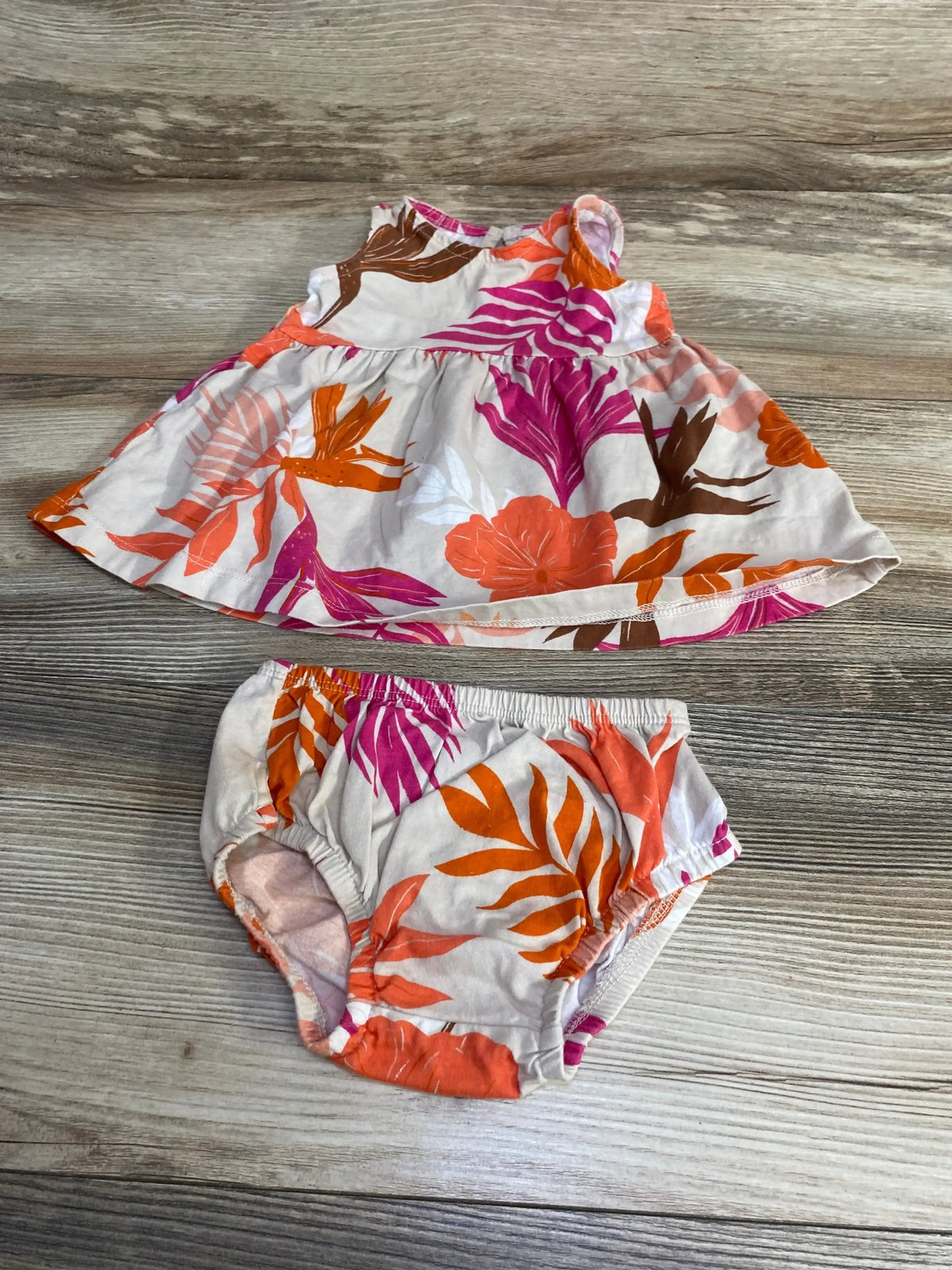 Flat lay of Carter's 2-piece baby dress and bloomers with orange and pink floral print on light wood background