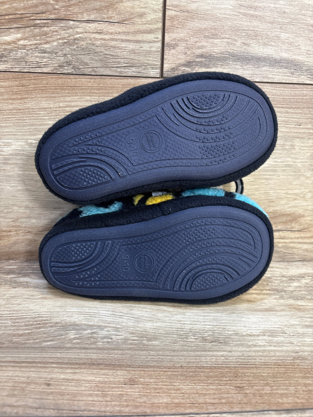 Bottom view of kids’ slippers with black rubber soles on wood floor