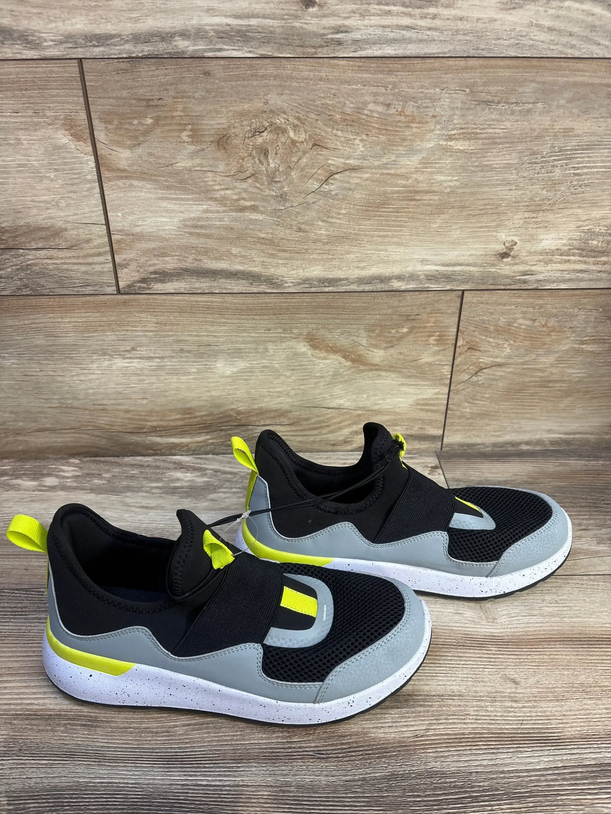 Three-quarter view of All In Motion Fern slip-on sneakers size 6Y in black grey with neon yellow accents on wood plank floor