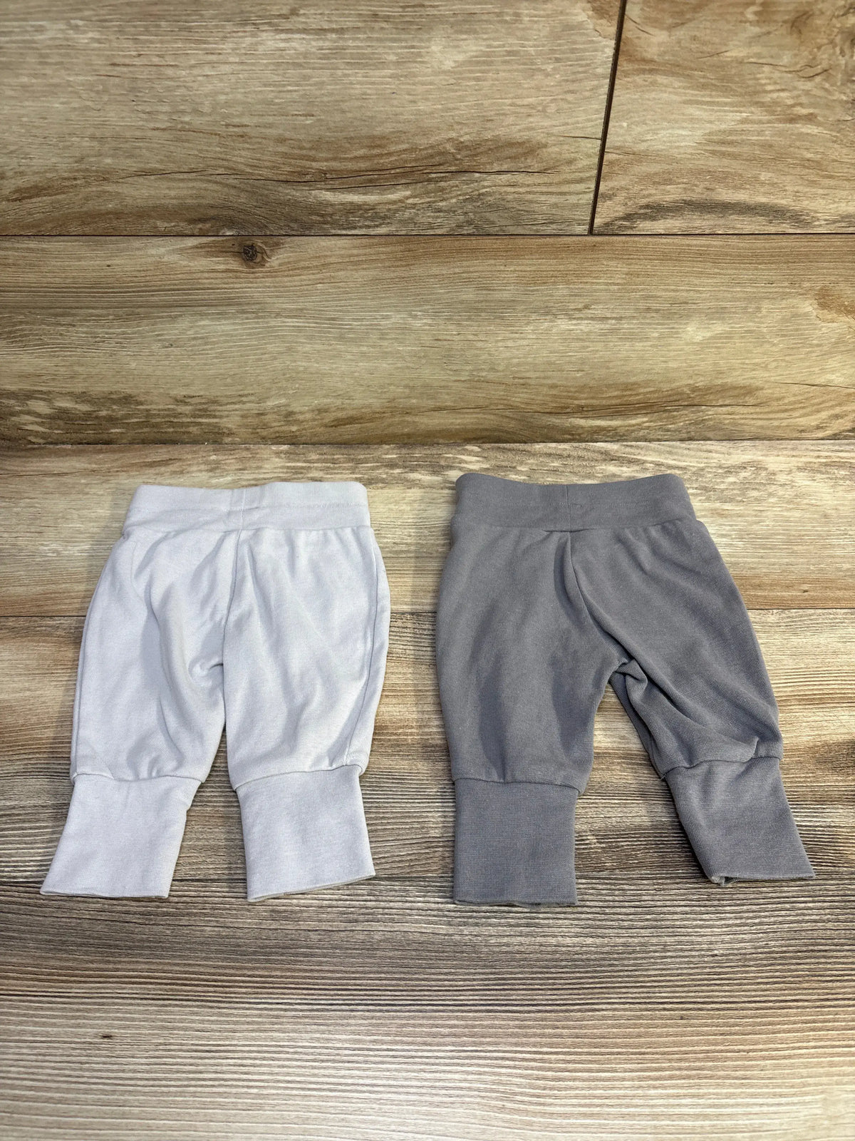 Top view of two Hanes baby pants in grey showcasing elastic waistbands and ribbed cuffs on a wood-grain floor