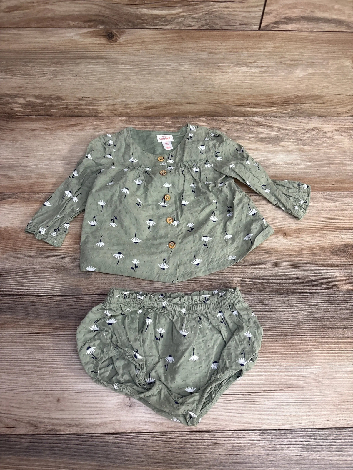 Flat lay of Cat and Jack 2pc tunic and bloomers set in sage showing white daisy print and wooden buttons on wood background