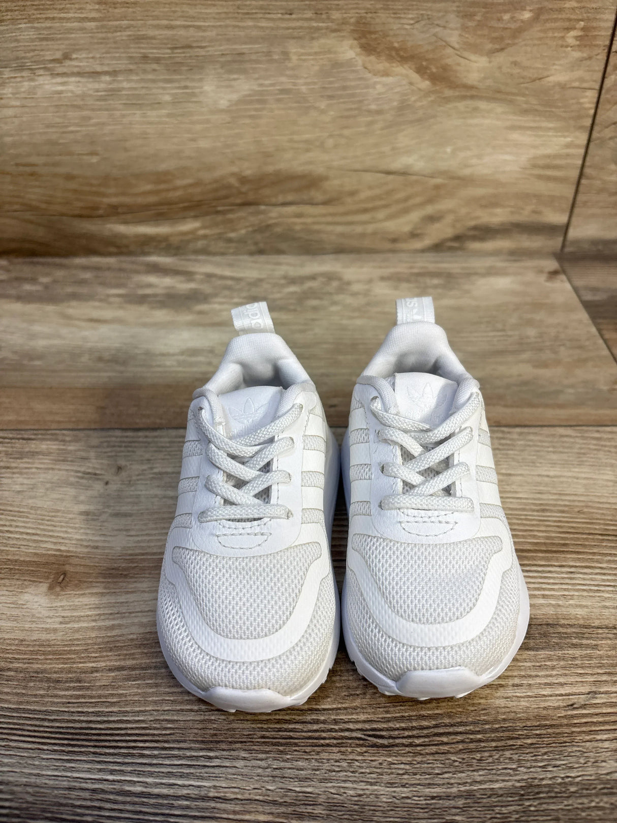 Top-front view of Adidas Multix Triple White sneakers size 4C showcasing mesh upper, laces and three stripes on wooden floor