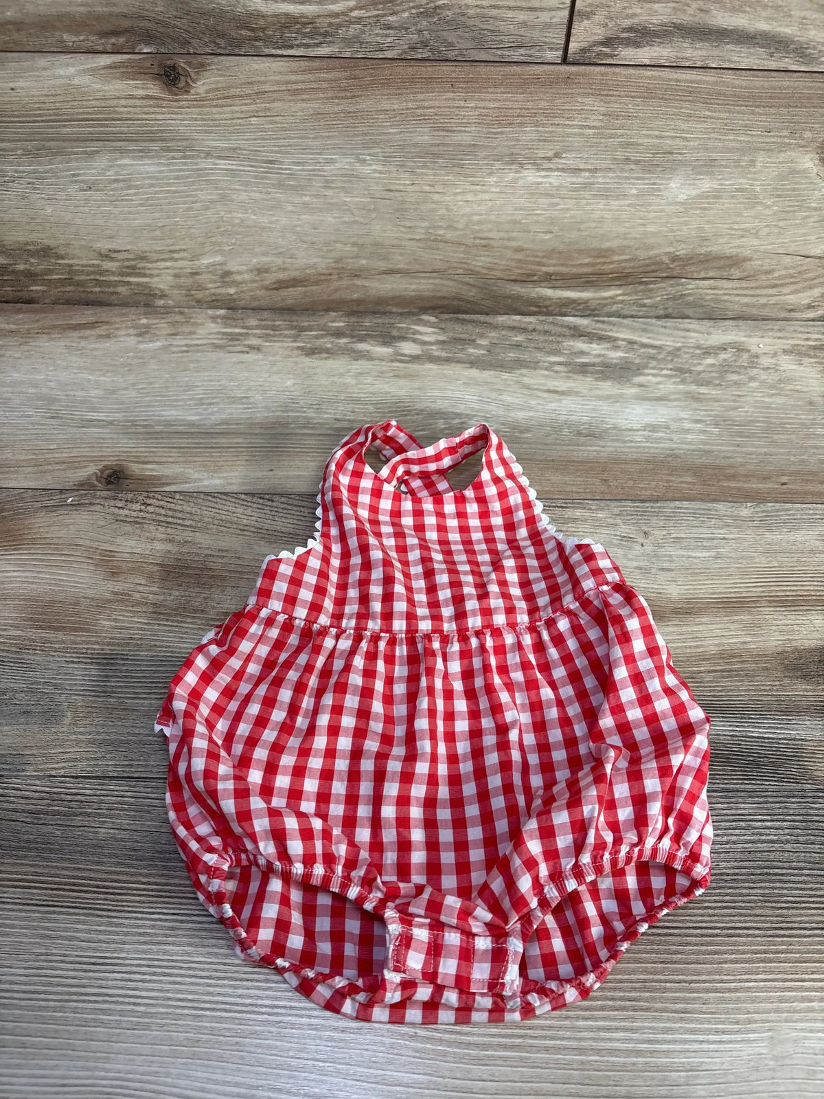 Top down view of red gingham bubble romper with ruffled halter neckline, gathered waist and elastic leg openings, wood floor