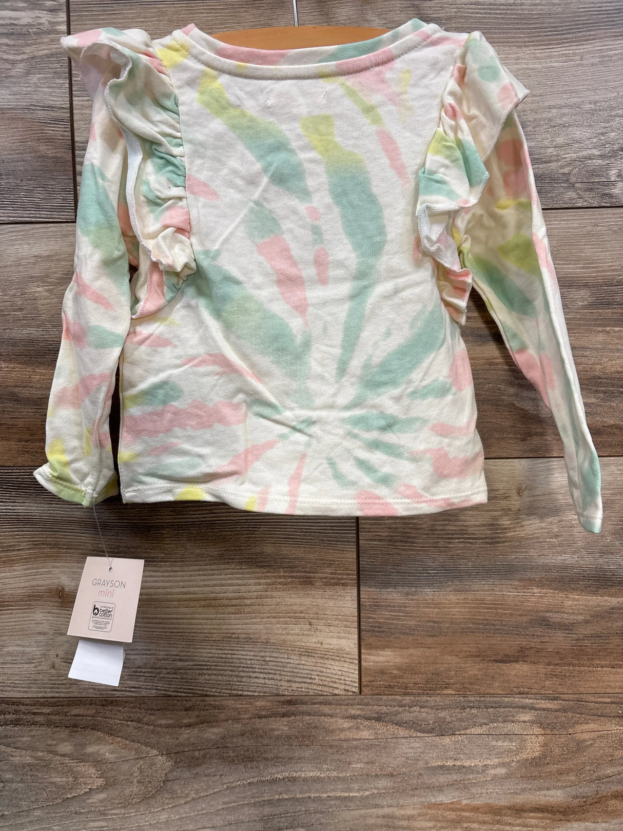 Grayson Mini girl's long sleeve tie-dye shirt with ruffle details on sleeves on wooden floor