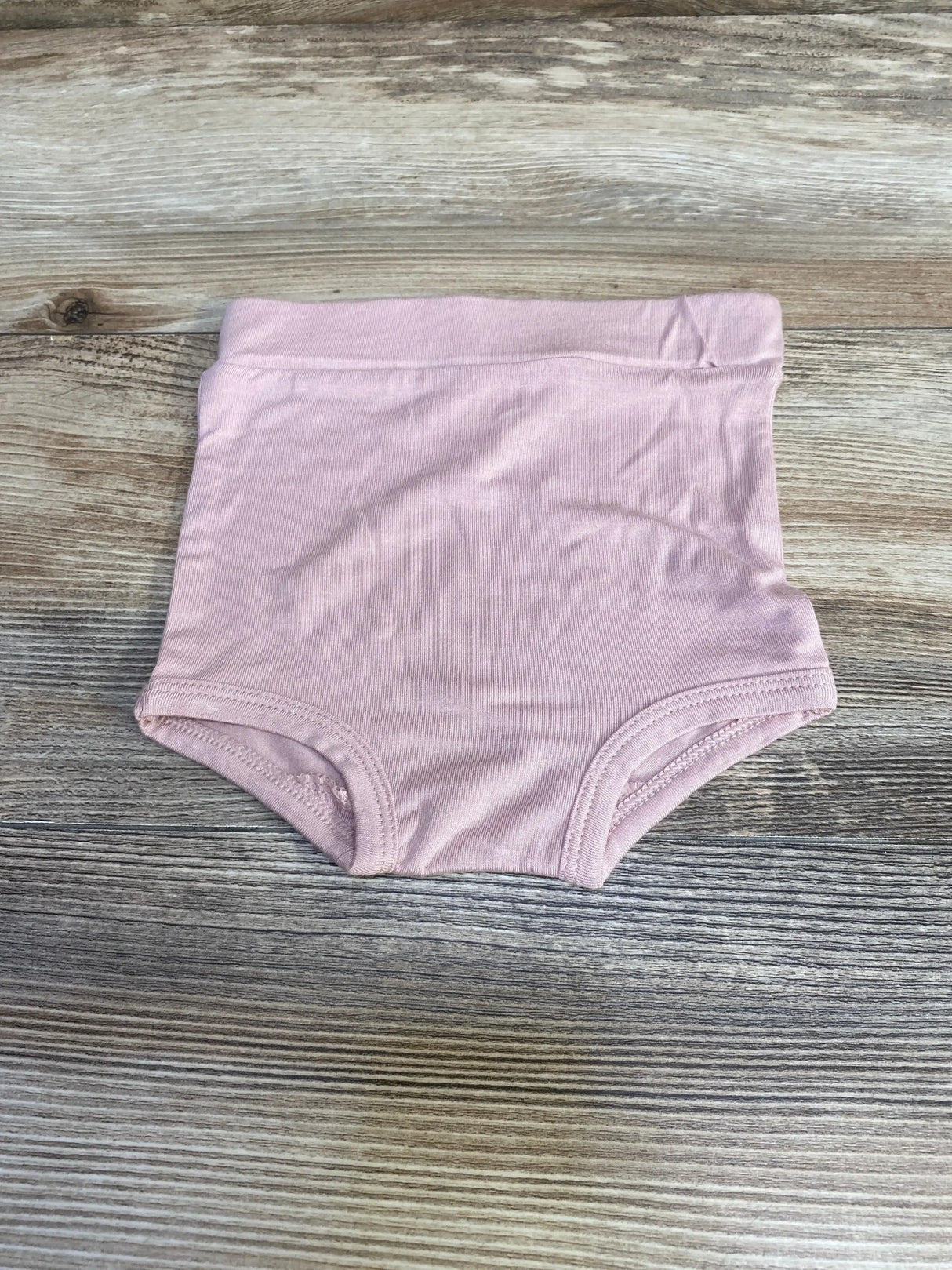 Top-down view of pink Kate Quinn baby bloomers showcasing high elastic waistband and full-coverage cut on wood background