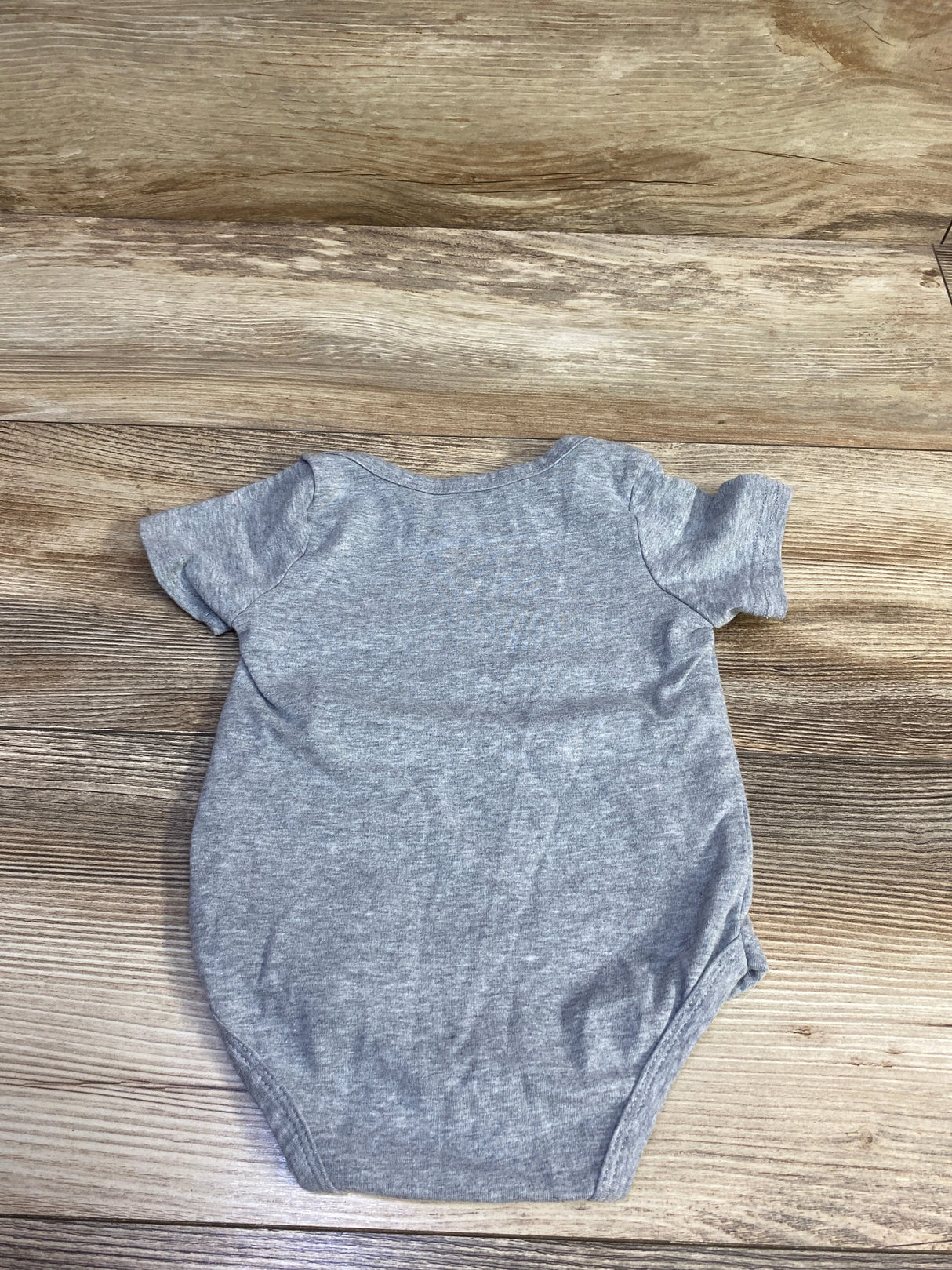 Back view of grey heather short-sleeve baby bodysuit showcasing fabric texture laid flat on wood background