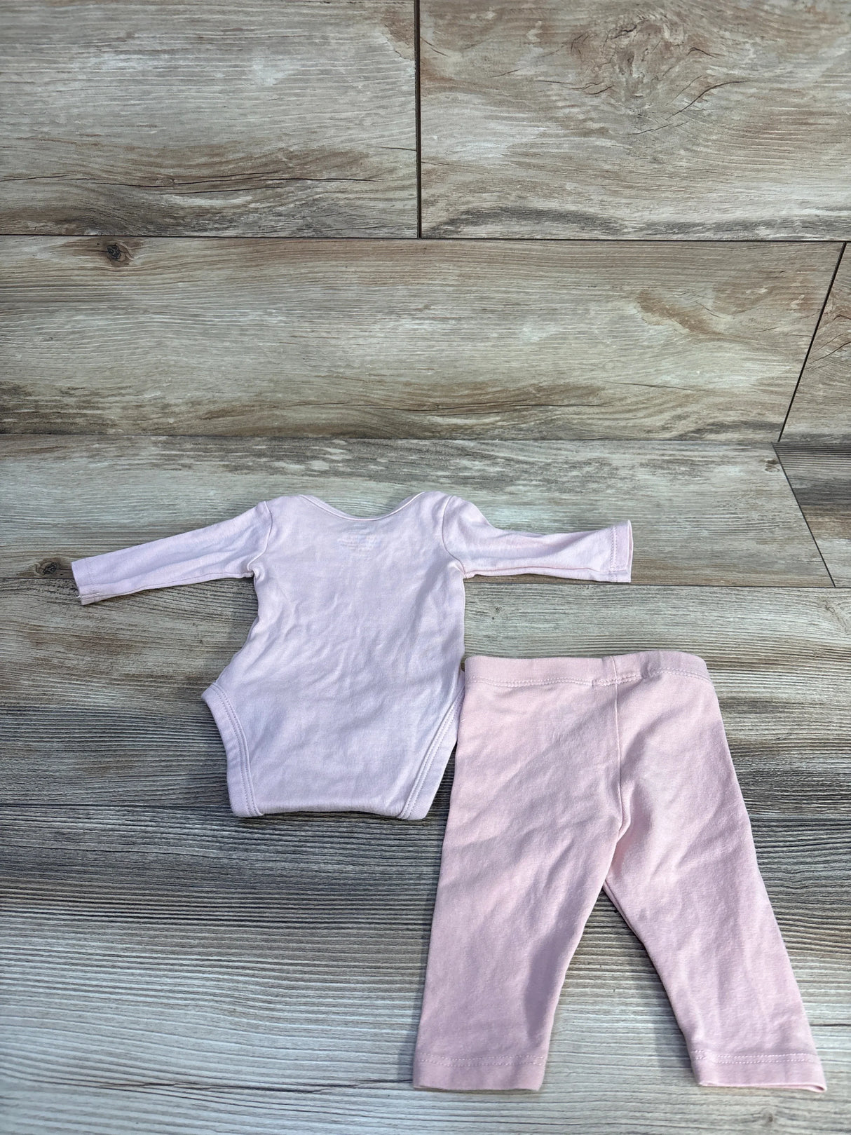Flat lay of preemie pink H&M two-piece bodysuit and pants showcasing long sleeves and elastic waist on wood plank background