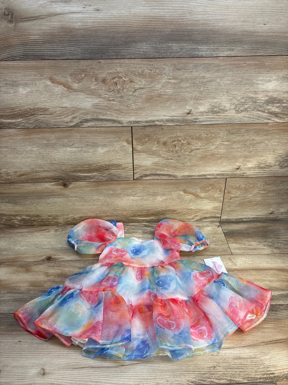 Colorful baby dress with puff sleeves and floral pattern on wood background