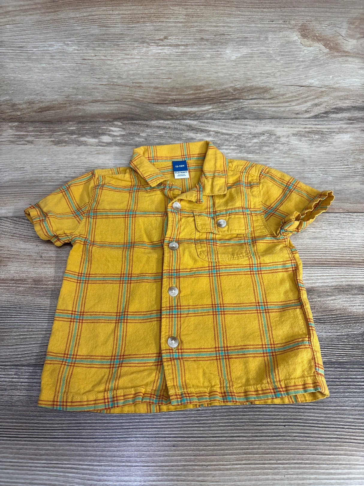 Yellow plaid baby shirt with short sleeves and front buttons on wooden background