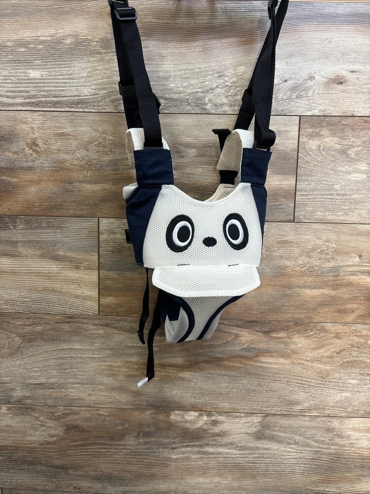 Front view of Pricexes Handheld Baby Walking Harness showing panda face, mesh panels, and adjustable black straps on wood