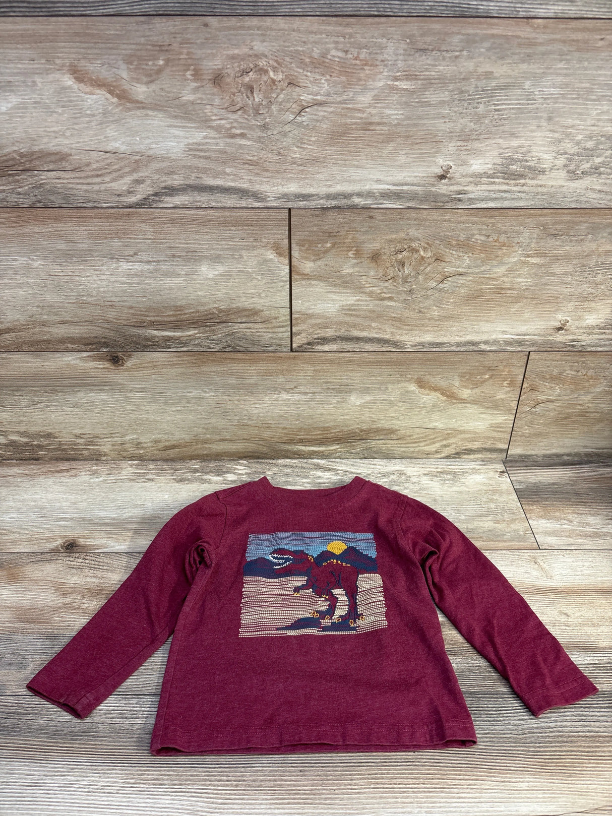 Front view of Kids Headquarters red long-sleeve toddler shirt showcasing a knitted dinosaur graphic on a wood plank background