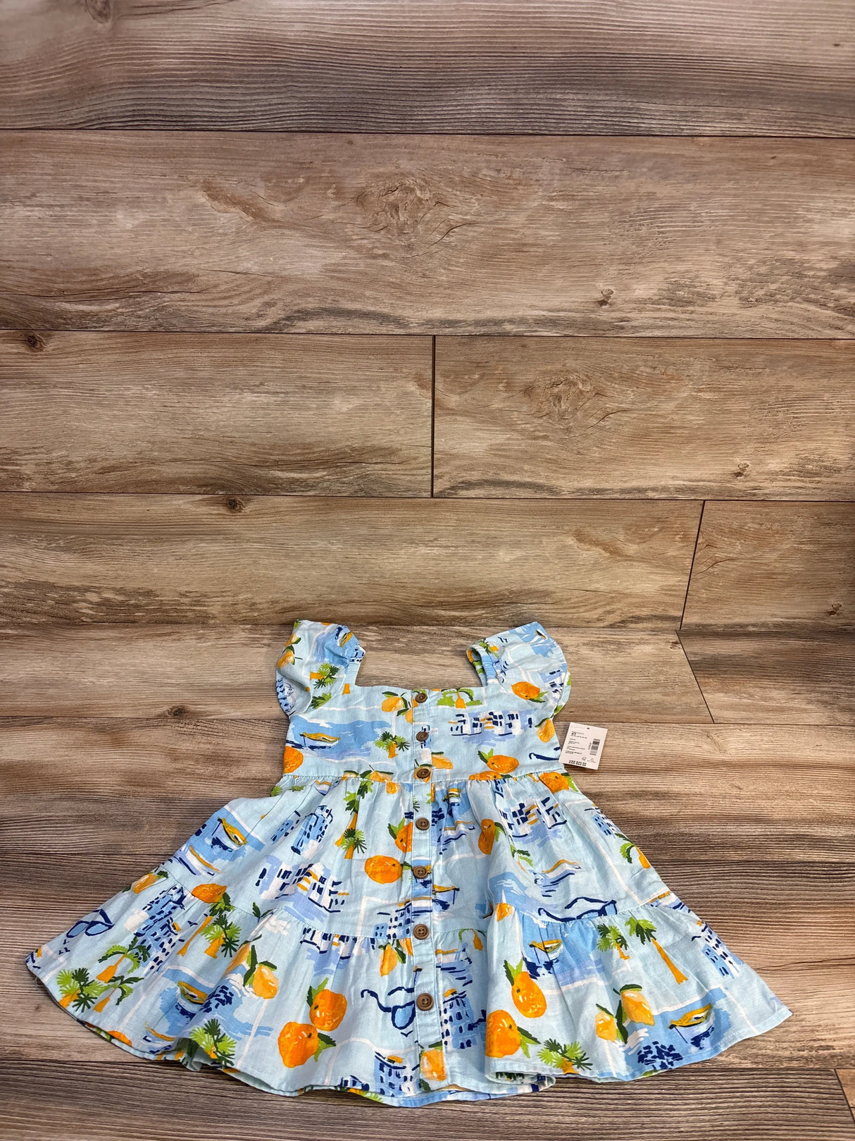 Blue baby dress with orange & palm tree print, button front, laid on wood floor