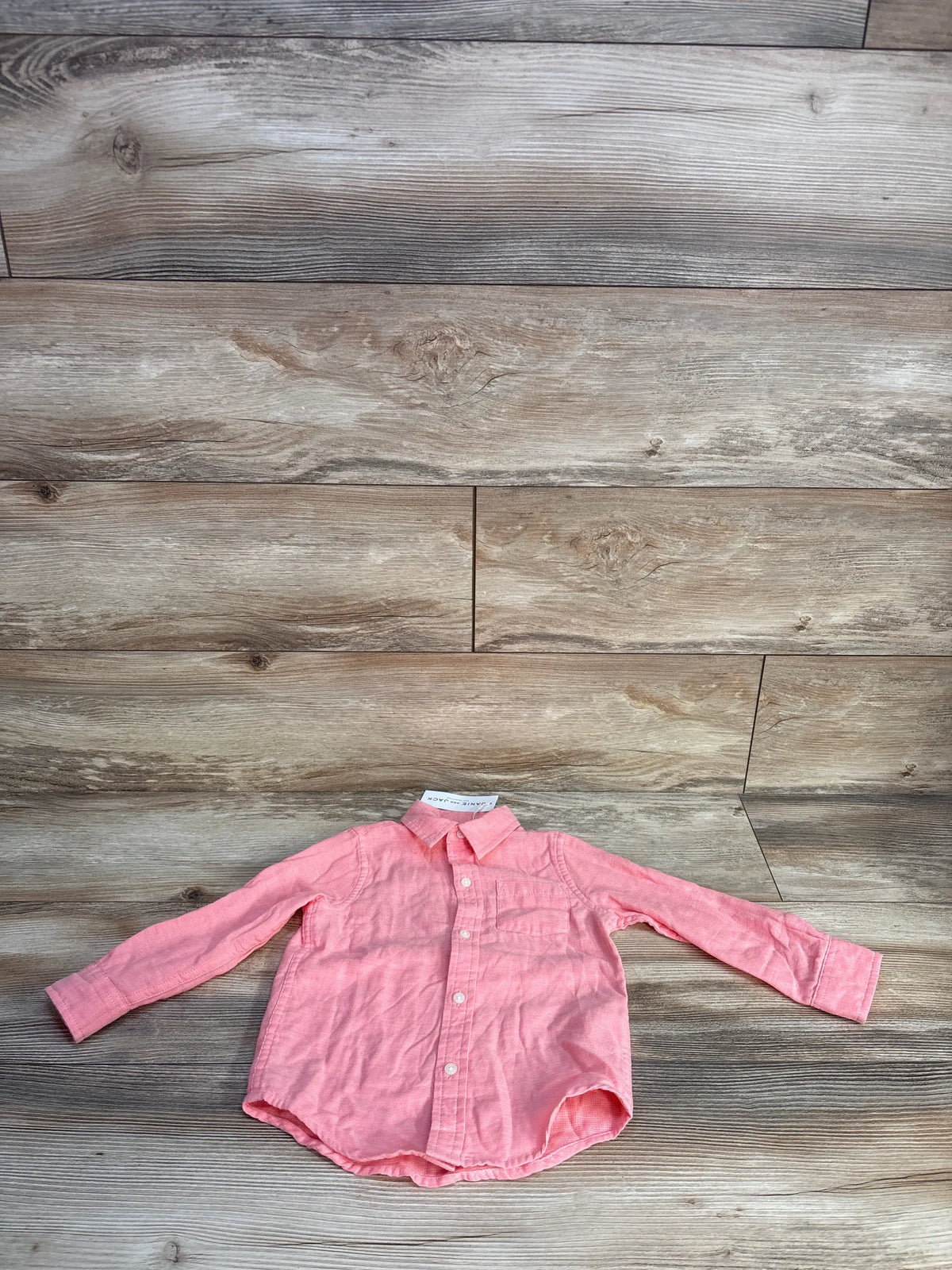 Front view of a pink Janie & Jack button-up shirt showcasing long sleeves, chest pocket, and curved hem on wood flooring