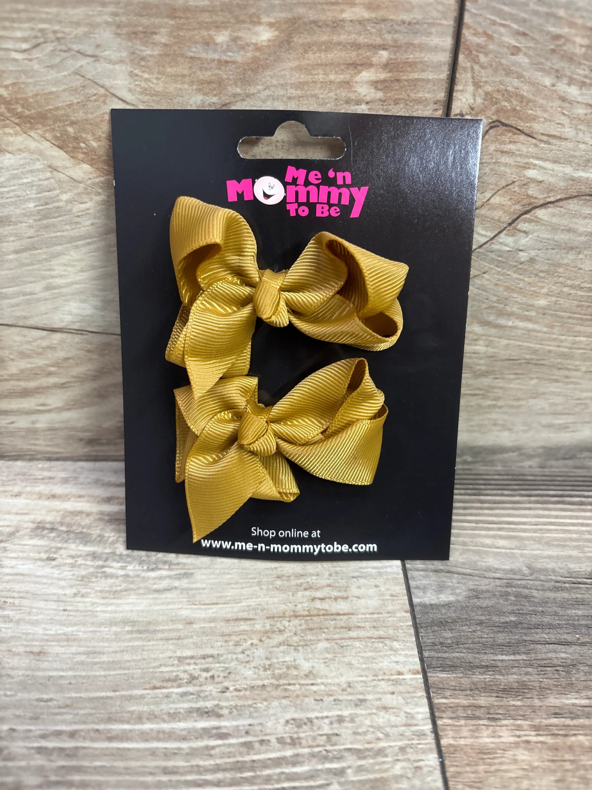 Two caramel-colored grosgrain hair bows on a black Me n Mommy To Be packaging card.