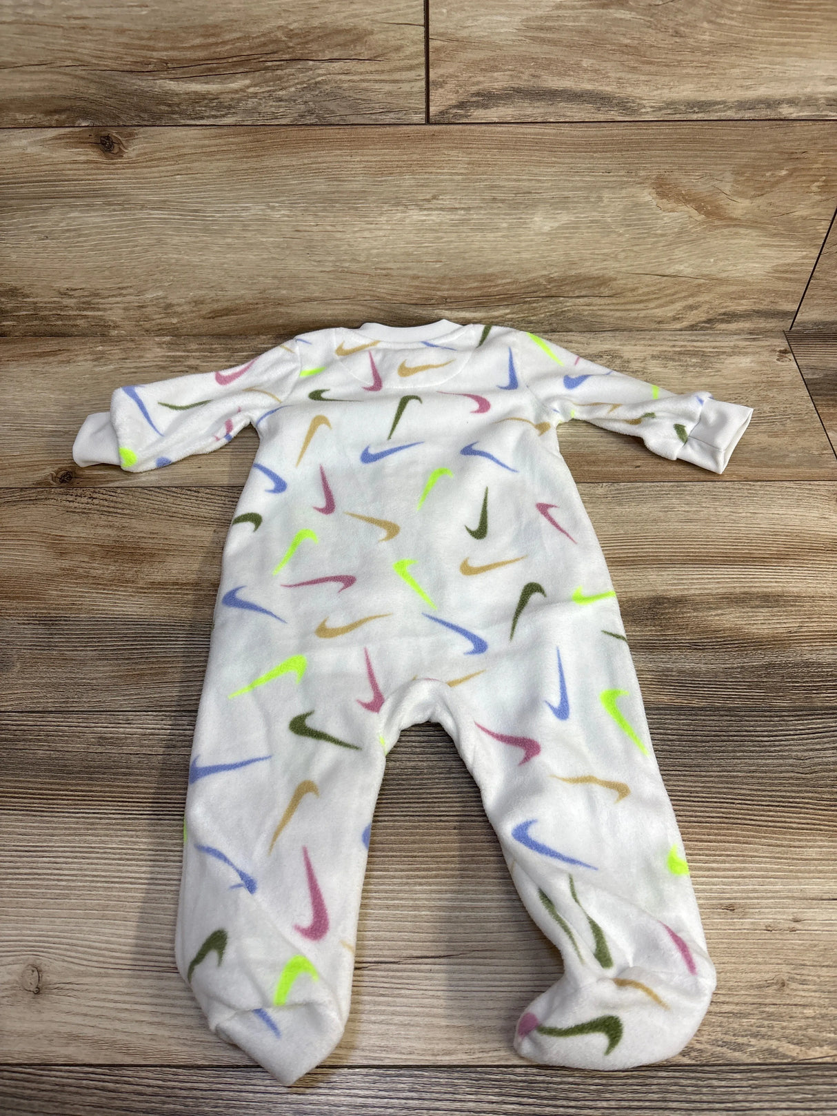 White baby sleeper with colorful Nike swoosh logos on wood floor