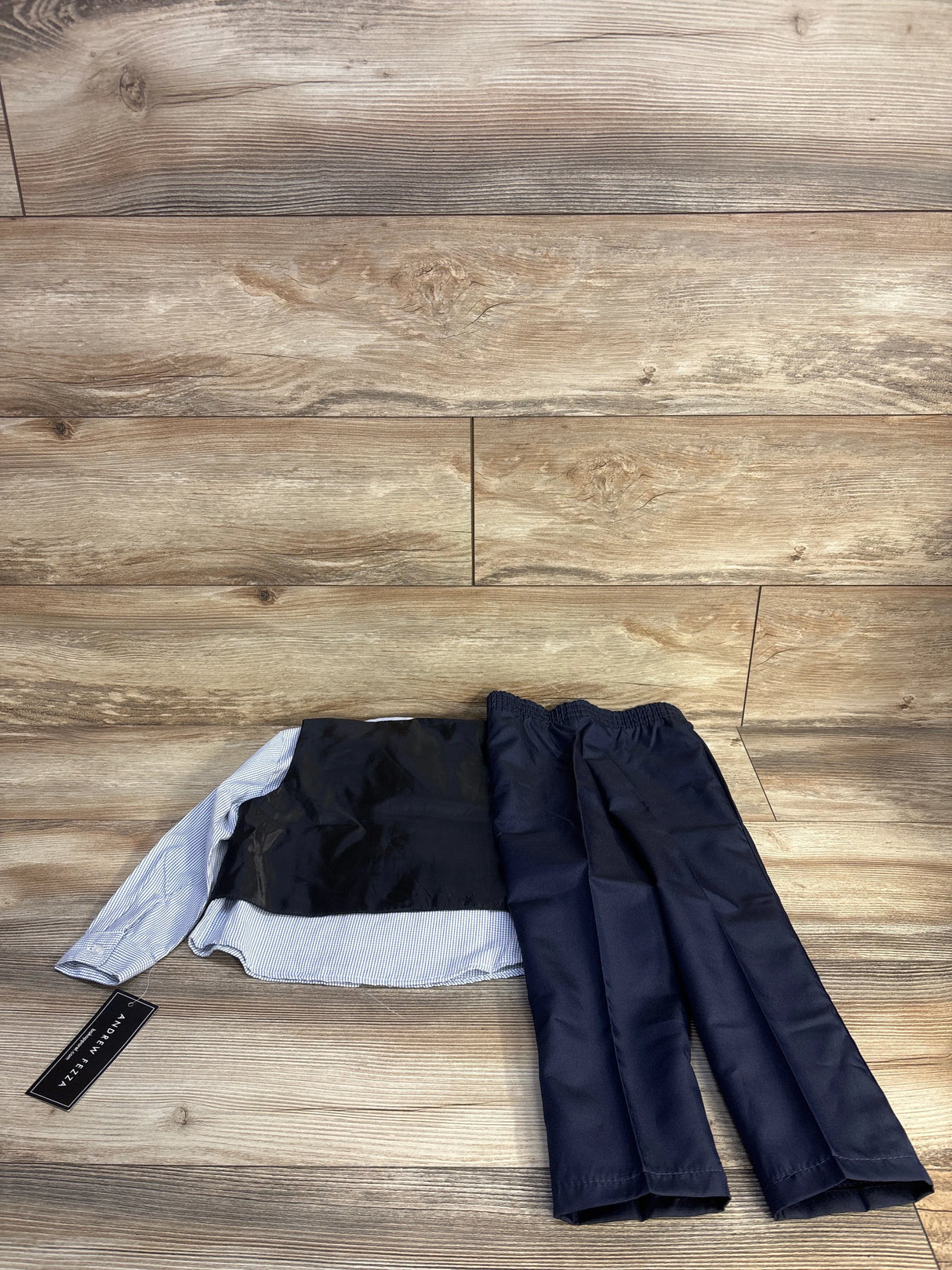 Flat lay of boys 4pc suit set (4T) with navy elastic-waist pants, light-blue striped shirt and black vest on wood floor