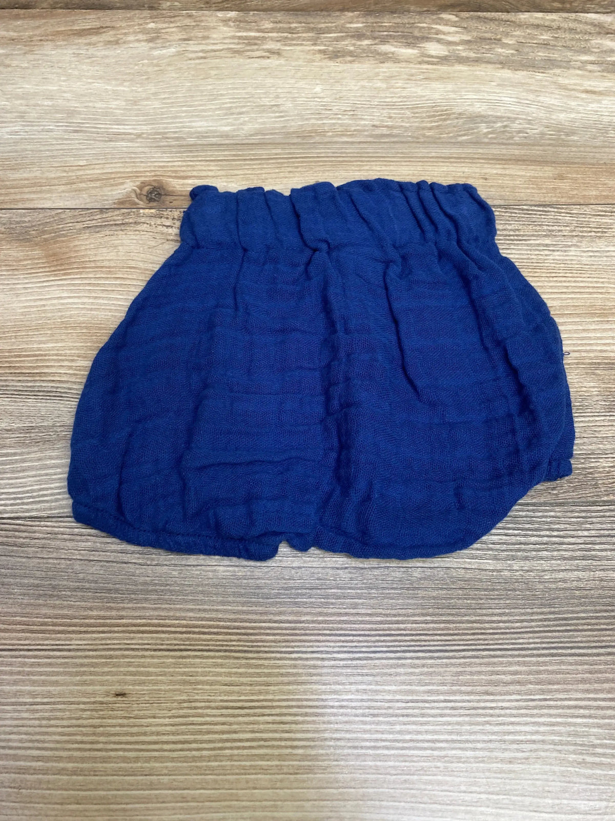 Top view of Emerson and Friends pull-on baby shorts size 0-3M in navy showing ruched elastic waistband and gauze texture on light wood background