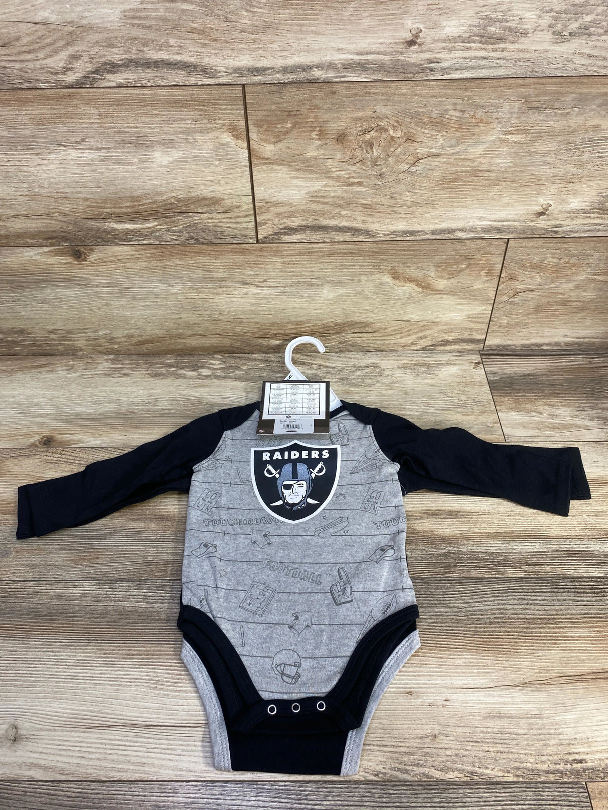 Oakland Raiders baby onesie with black sleeves on wood floor