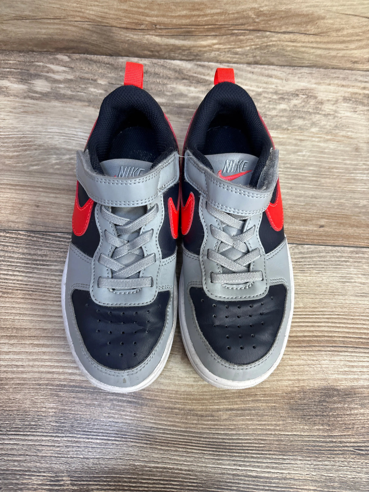 Kids' Nike sneakers with gray, black, and red accents on wood floor