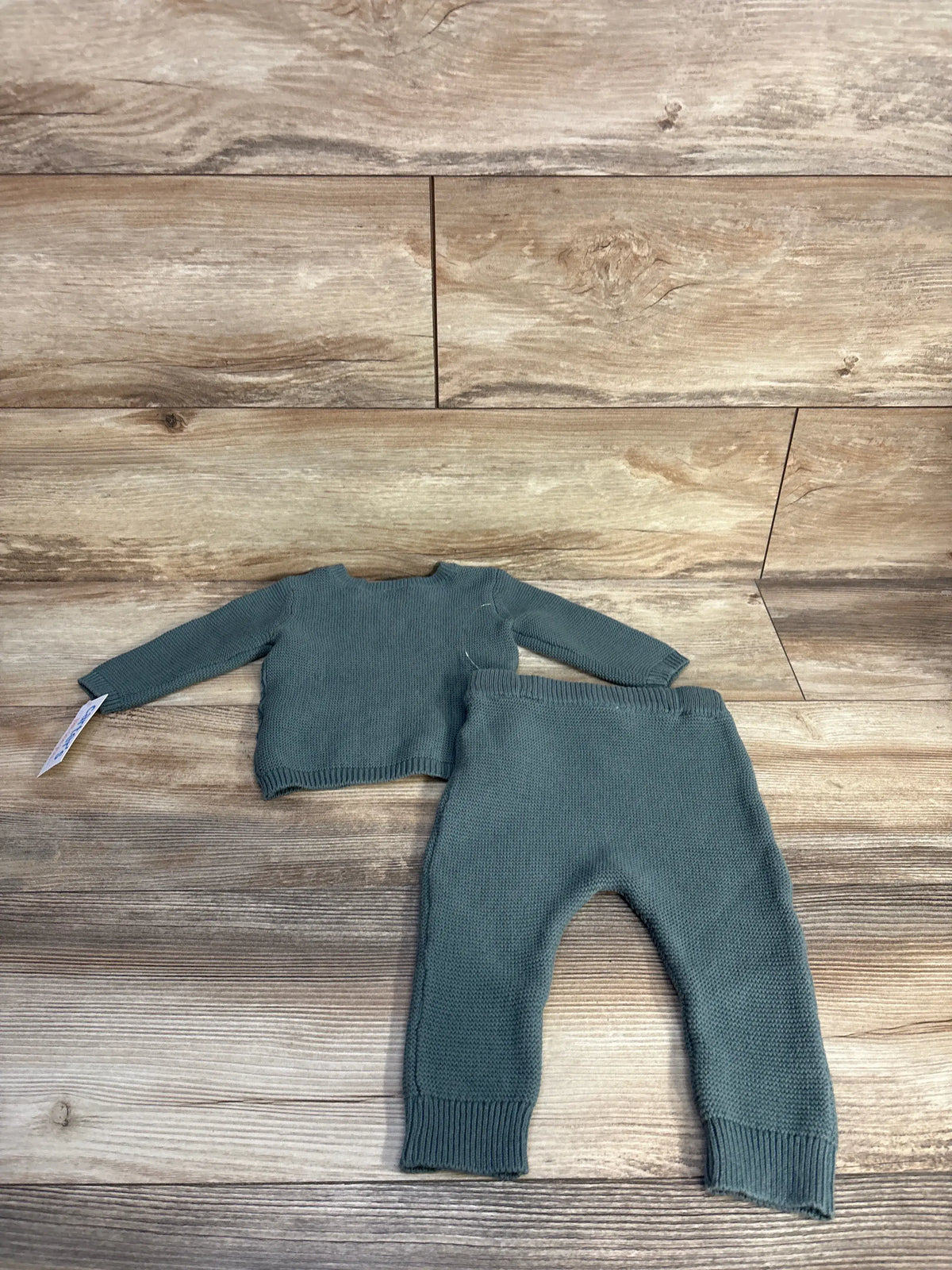 Top view of Carter’s two-piece green knit sweater and leggings set showcasing ribbed cuffs on a wood background