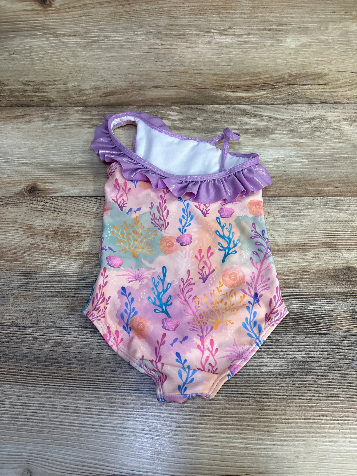 Front view of purple Disney The Little Mermaid one-piece swimsuit showcasing ruffled neckline and coral pattern on wood background