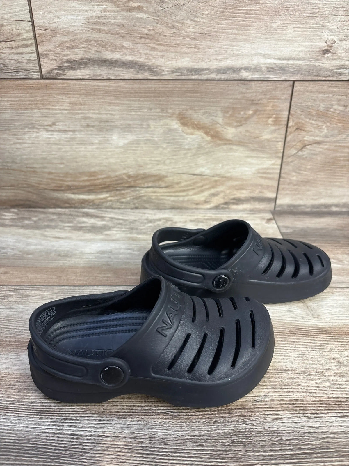 Three-quarter view of Nautica River Edge clogs in black showing vented upper, heel strap and textured footbed on wood floor
