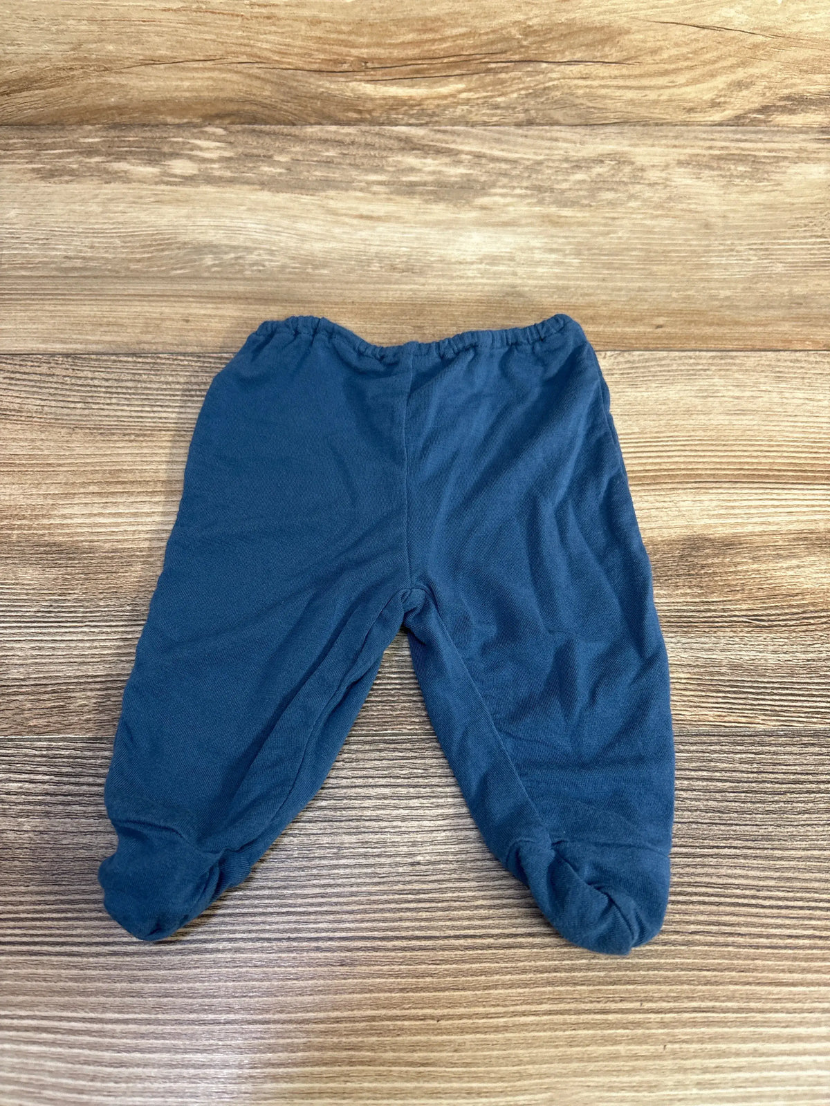 Front view of Kickee Pants blue bamboo footed pants showcasing covered feet and elastic waistband on wood-grain background