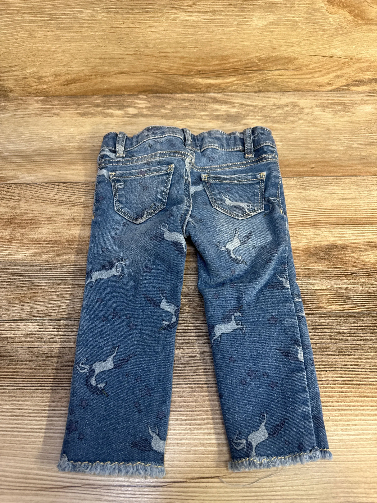 Children's blue denim jeans with unicorn print and frayed hems on wood background
