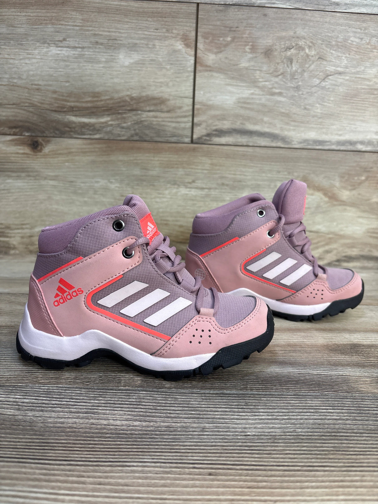 Side view of Adidas TERREX Hyperhiker Mid mauve hiking sneakers size 11C with white three stripes and rugged black sole on wood