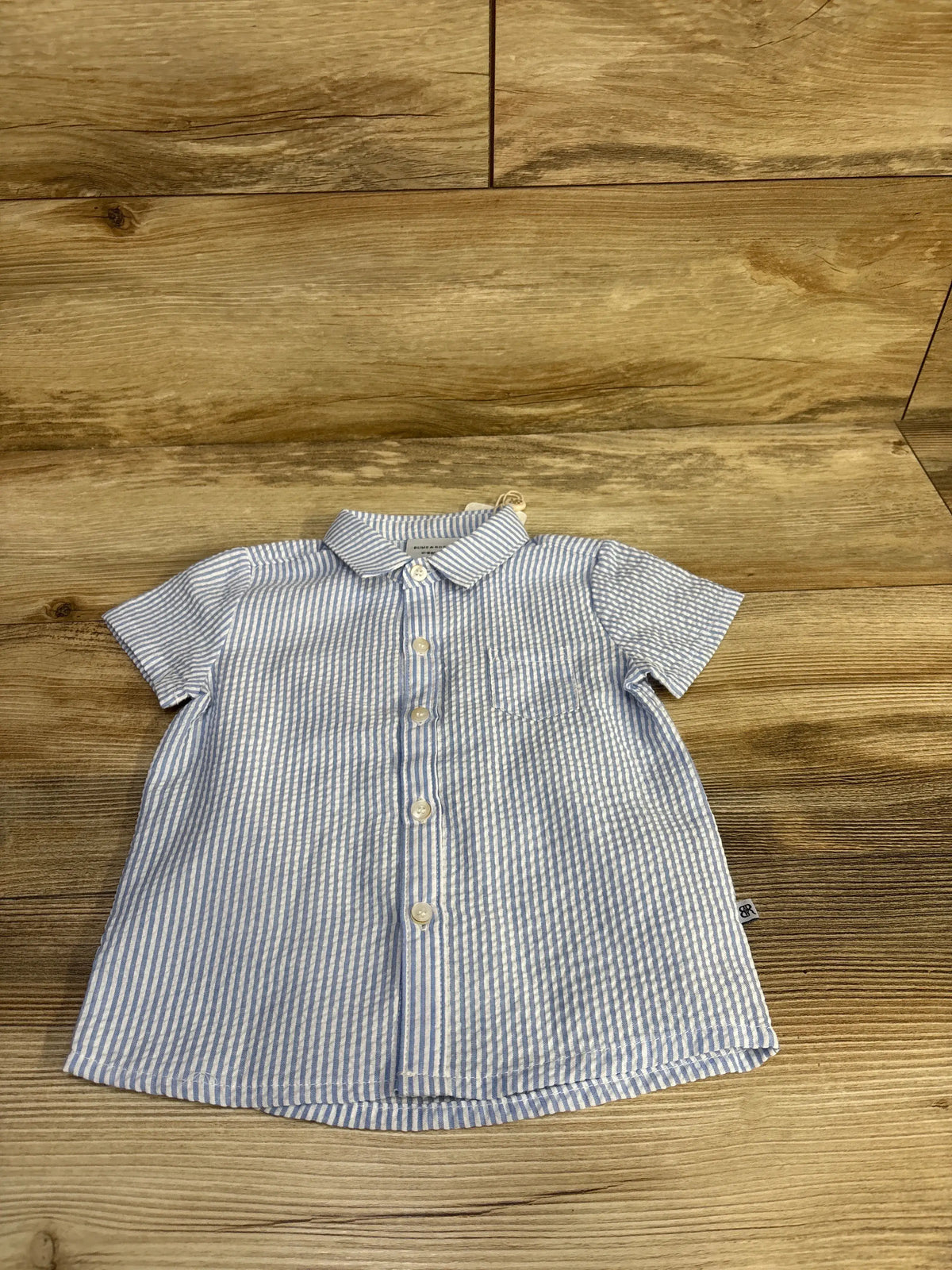Front flat lay of light blue seersucker striped baby button-up shirt with front buttons on wood background