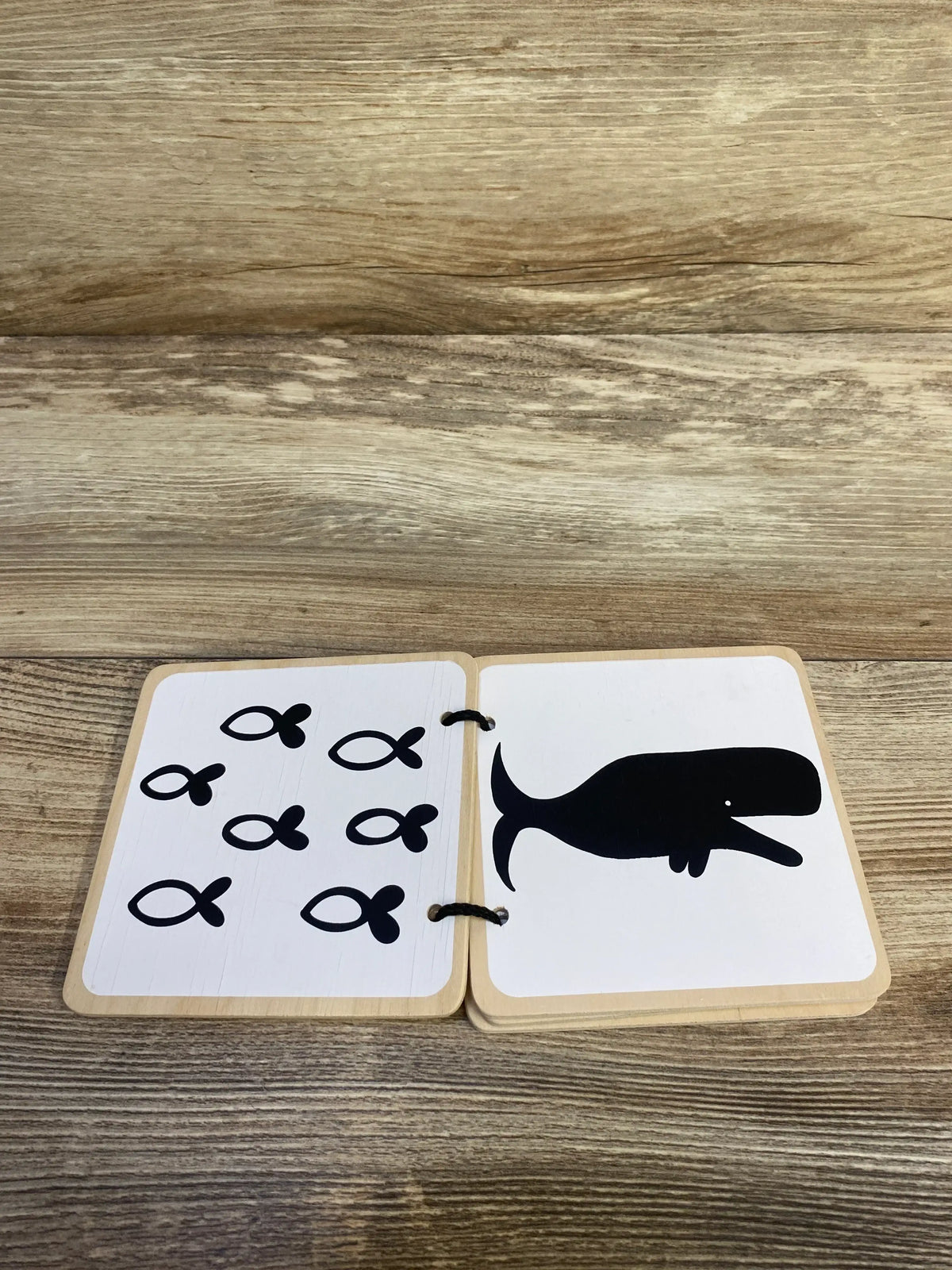 Open view of Lovevery Wooden Book showcasing high-contrast black and white pages with fish and whale illustrations on wood plank floor
