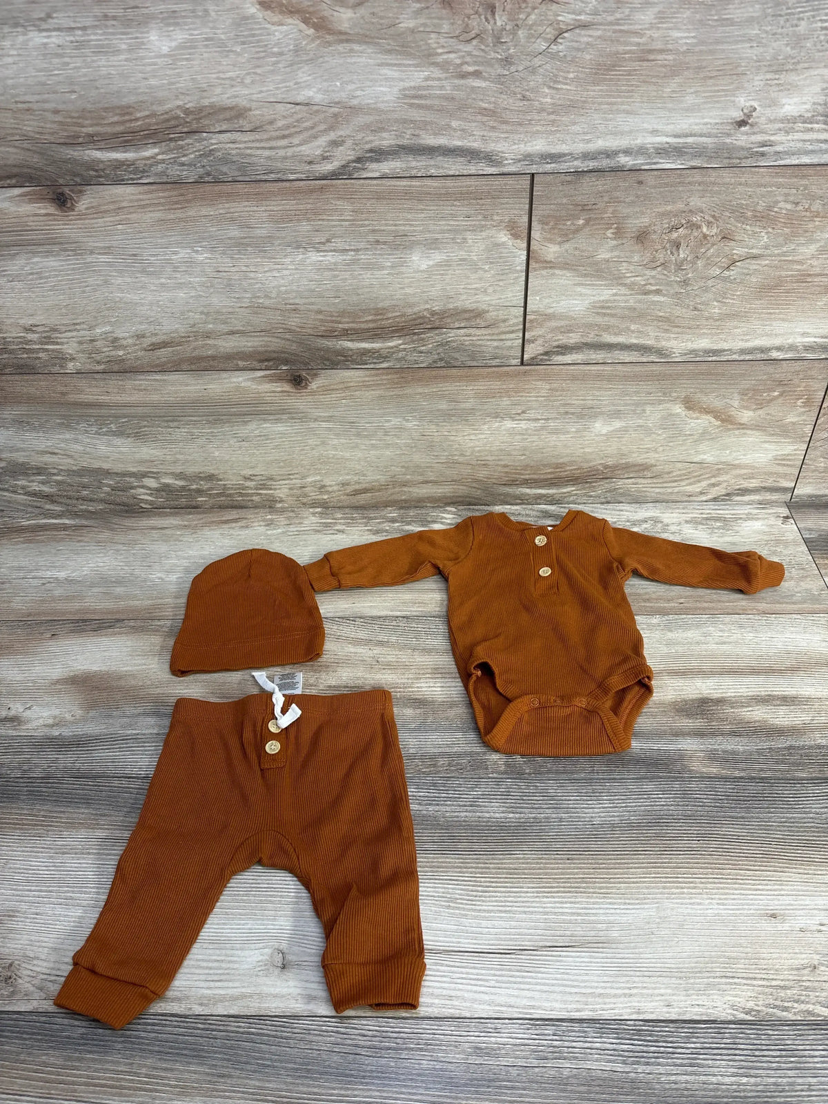 Rust orange ribbed baby outfit set with hat, bodysuit, and pants on wood background
